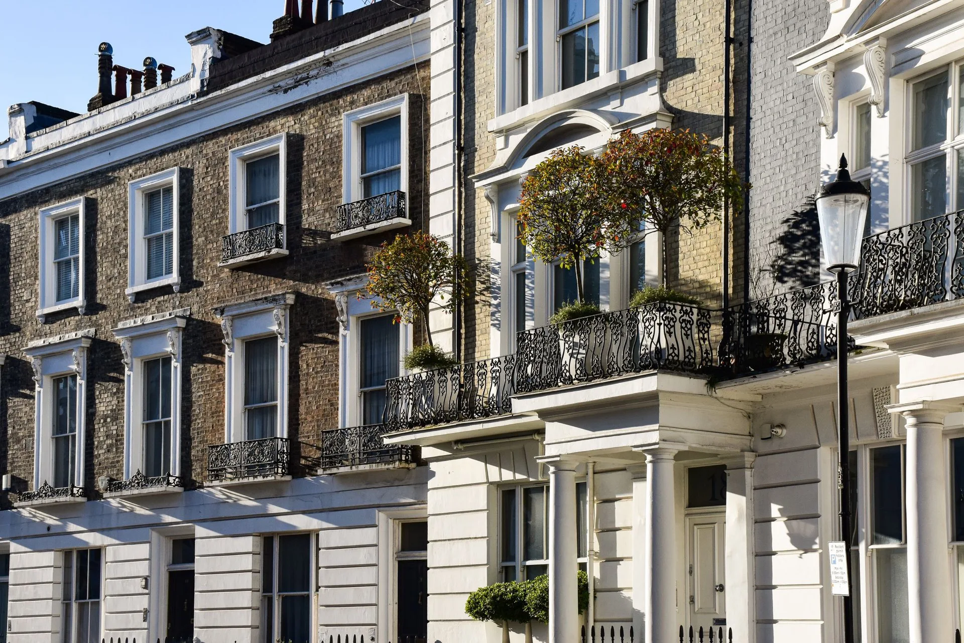 Row of prime central London period townhouses with ornate iron balconies, porticos and bay trees in golden afternoon light, representative of the high-value residential property financed by high net worth mortgages